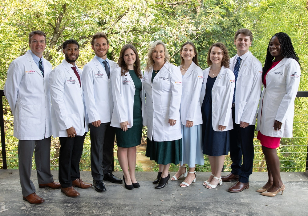 Group of medical students and faculty in white coats posing outdoors