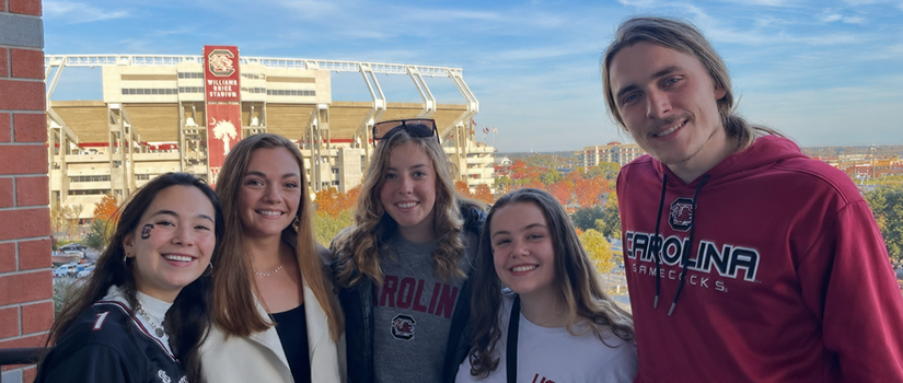 Five University of South Carolina students pose together with Williams-Brice Stadium in the background.