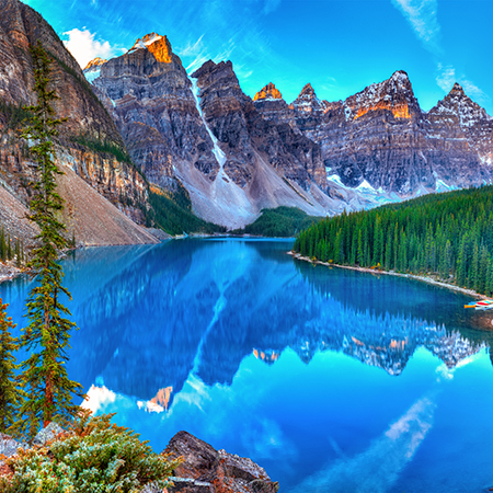 A breathtaking view of Moraine Lake in Banff National Park, Canada, featuring crystal-clear turquoise water reflecting the surrounding snow-capped mountains and evergreen forest under a bright blue sky.