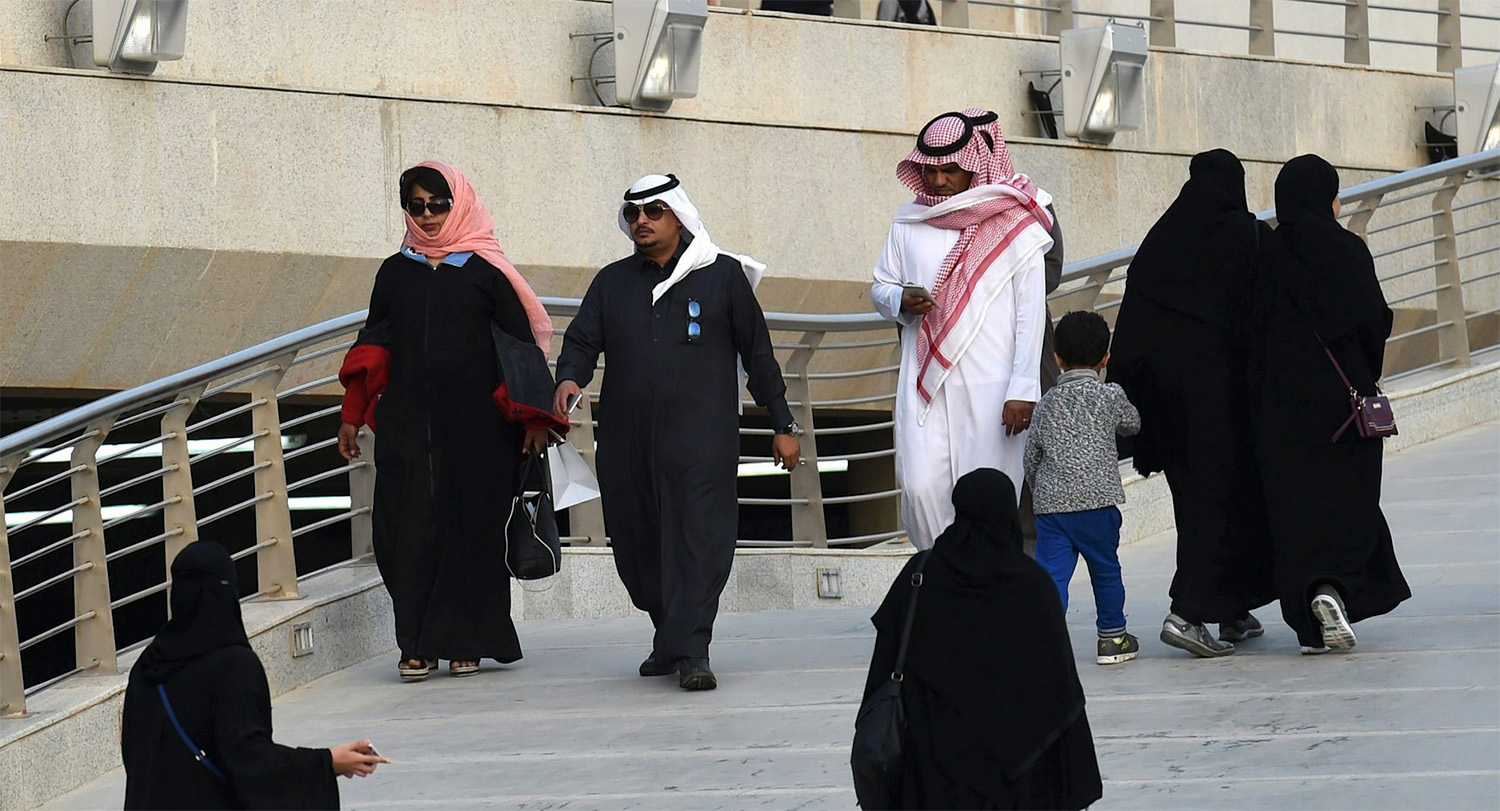 Saudi citizens wearing traditional loose robing in black and red stroll an elevated sidewalk