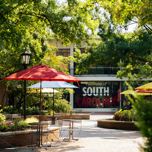 sign reading 'university of south carolina' seen through a patio with trees and tables